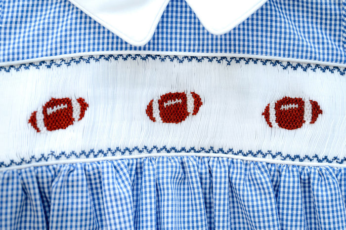Boy's blue gingham game day bubble featuring a hand-smocked football panel and easy snap closure