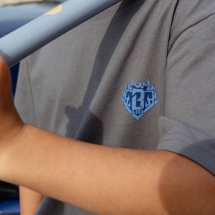 Close-up of blue BL101 flame diamond chest graphic on gray youth Flame Thrower tee, baseball bat casting shadow across chest.