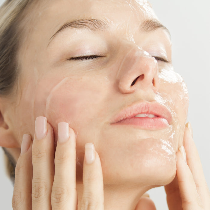 Woman gently applying hydrating face mask for radiant skin care routine, showcasing smooth texture and glowing complexion.