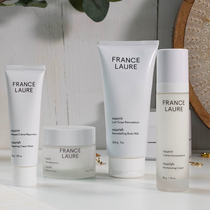 France Laure nourish skincare collection: repairing cream mask, body milk, harmonizing cream on white surface with green leaves