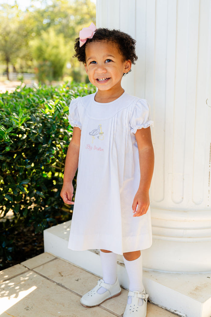 A little girl wearing the white big sister stork dress