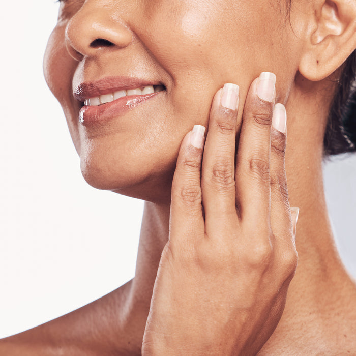 Woman gently touching smooth, radiant skin on her cheek, showcasing natural beauty and healthy skincare routine