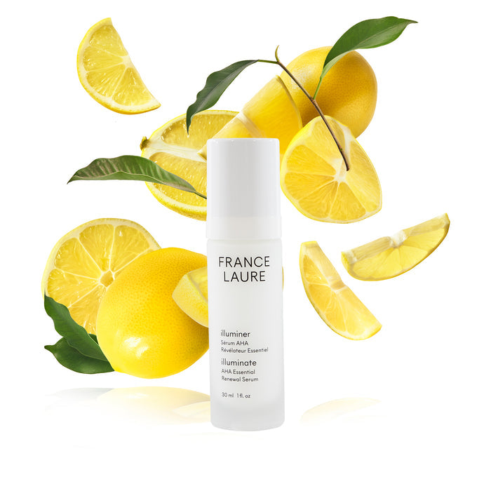 France Laure Illuminate AHA Essential Renewal Serum bottle with fresh lemon slices and green leaves, showcasing brightening skincare benefits.