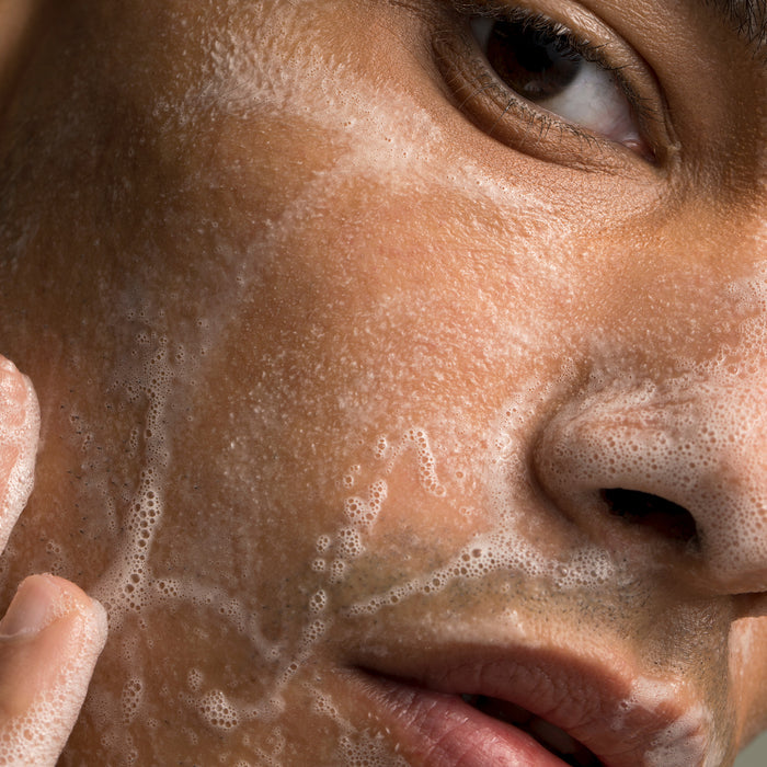 Close-up of person gently massaging foaming facial cleanser onto skin, showcasing gentle skincare routine for all skin types