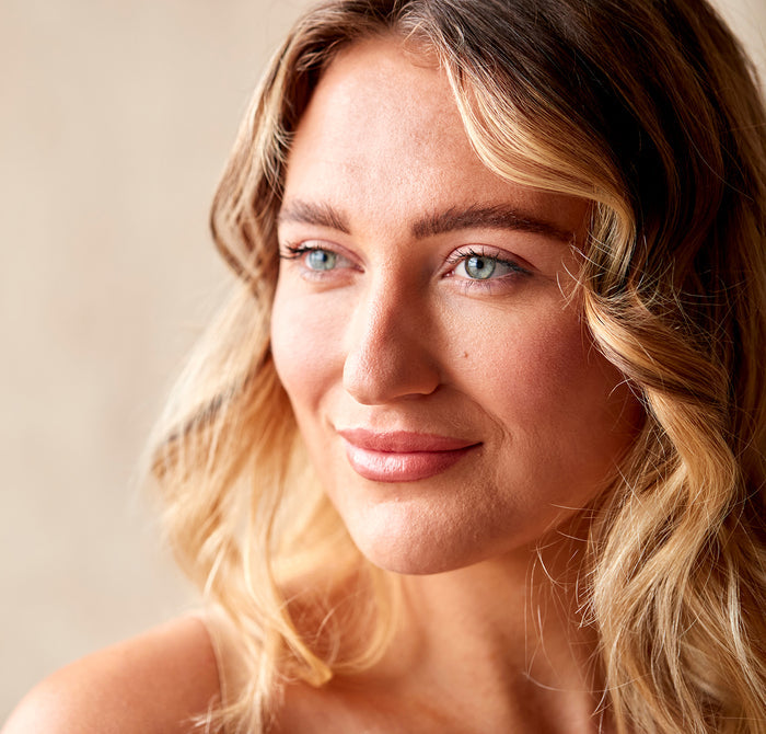 Woman with radiant, healthy skin and soft wavy blonde hair, showcasing natural beauty and skincare results