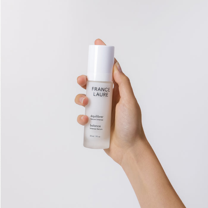 Hand holding France Laure Balance Intense Serum bottle, 30ml skincare product for all skin types, minimalist white design