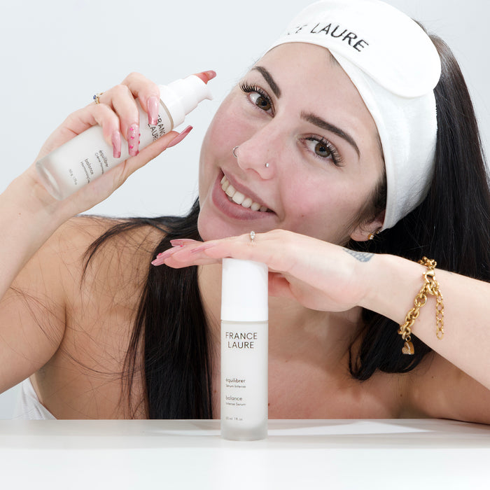 Woman holding France Laure Balance Intense Serum and Harmonizing Cream, showcasing skincare routine with white headband and manicured nails.