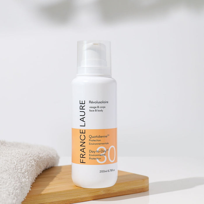 France Laure Révolusolaire SPF 30 face & body sunscreen with daily environmental protection, shown on wooden tray beside towel