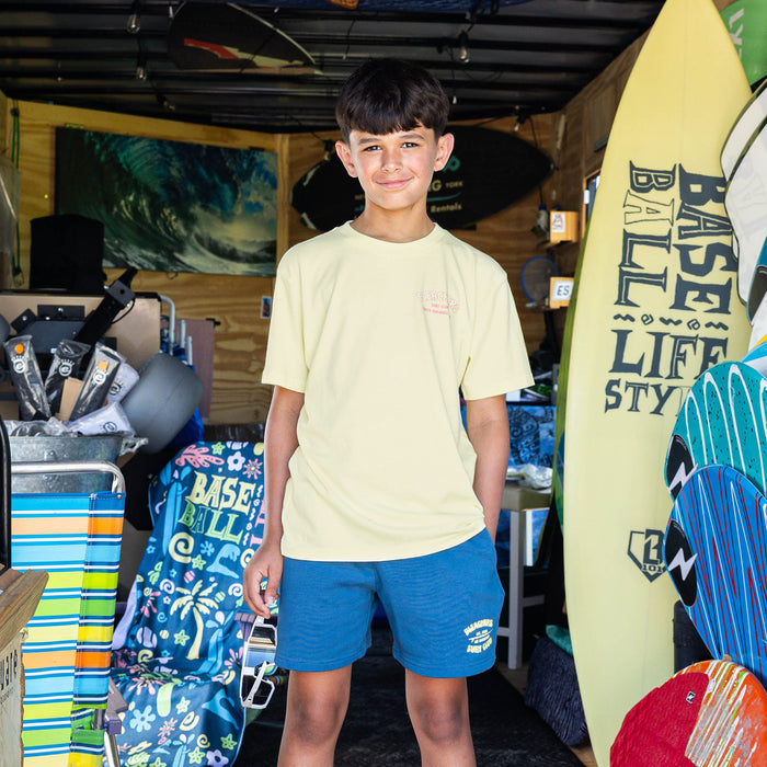 Youth model wearing yellow youth graphic tee with "Bleachers Surf Club" design