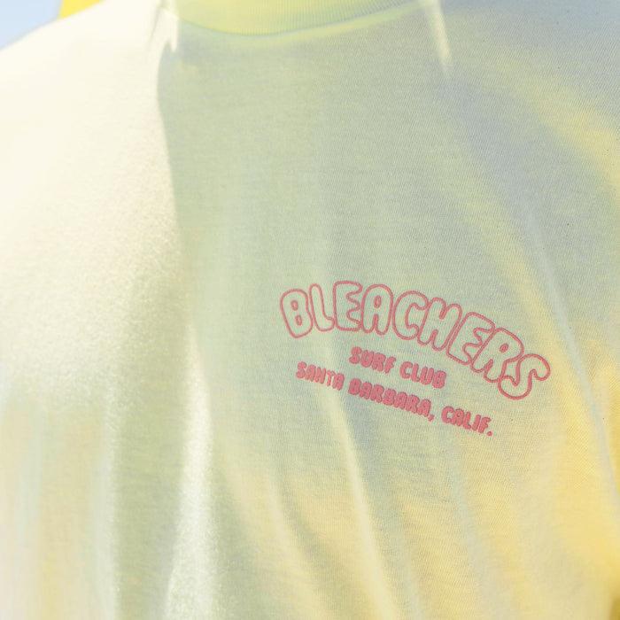 Youth model wearing yellow youth graphic tee with "Bleachers Surf Club" design