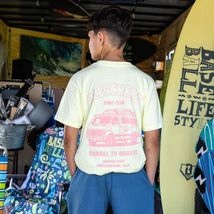 Youth model wearing yellow youth graphic tee with "Bleachers Surf Club" design