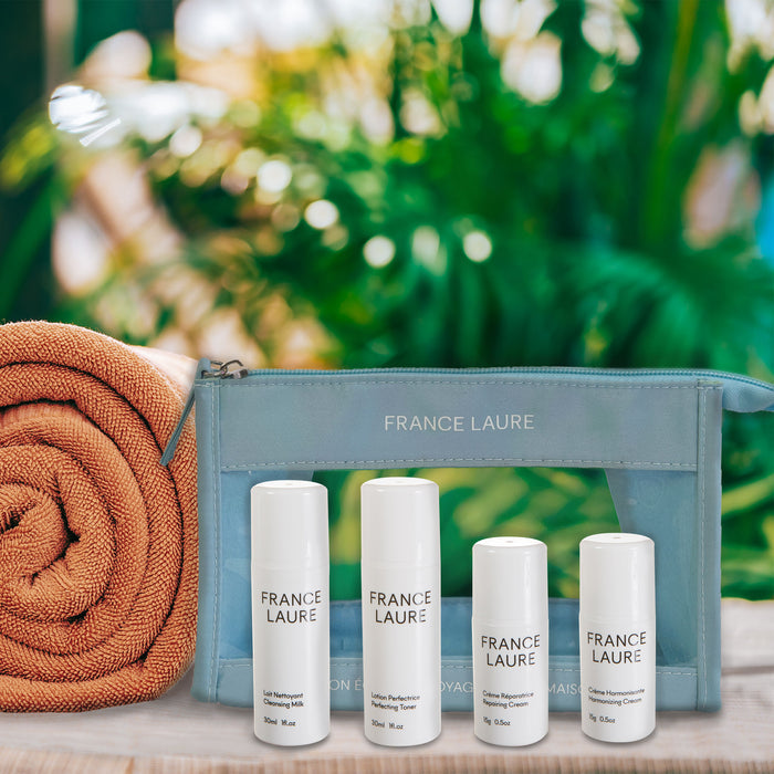 France Laure travel skincare set with cleansing milk, toner, repairing cream, and harmonizing cream in a blue pouch beside a towel, ideal for all skin types.