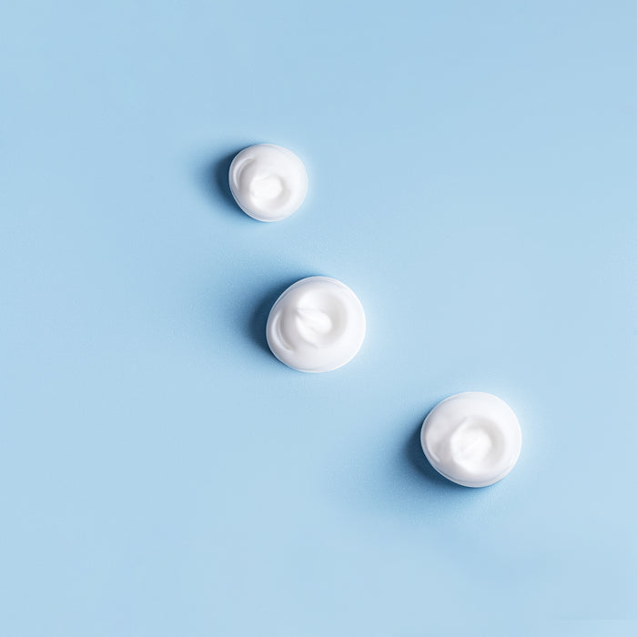 Three dollops of creamy white skincare product on a soft blue background, showcasing smooth texture for all skin types.
