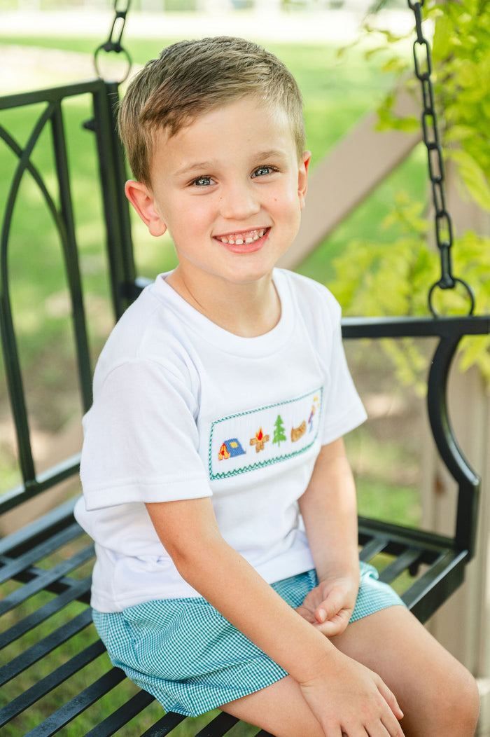 Boy wearing Camping Smocked Beau T-Shirt and Shorts Set, sitting on porch swing outdoors