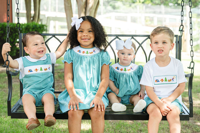 Three children sitting on porch swing wearing matching Ruth and Ralph smocked camping outfits