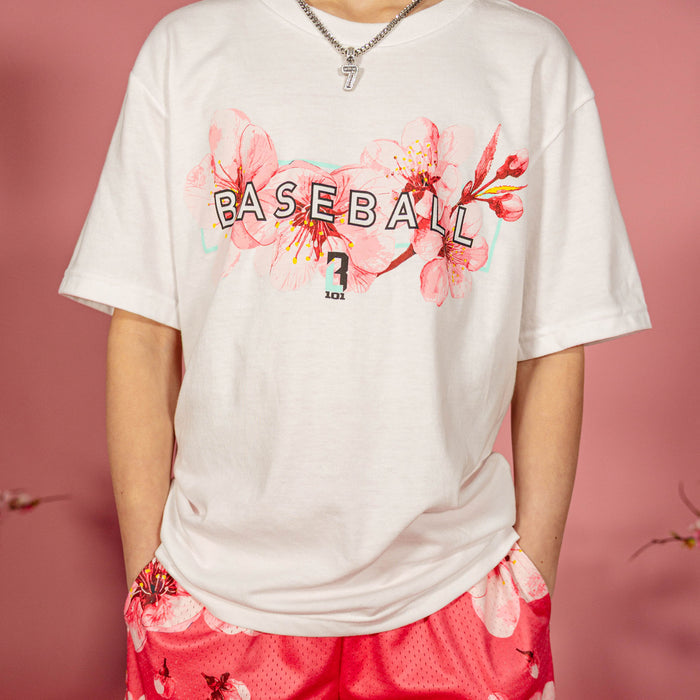 Close up of the cherry blossom Baseball graphic on a white BL101 tee worn by a young boy with pink floral shorts against a pink background