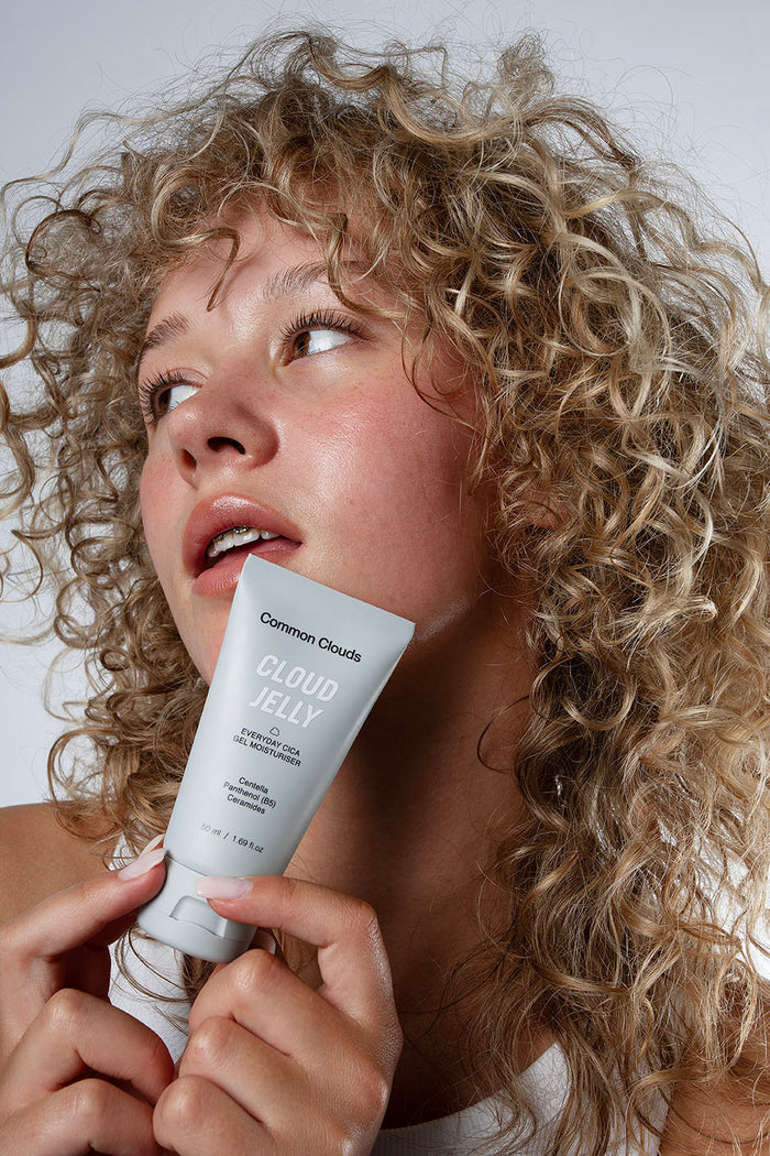 A girl holding a Cloud Jelly moisturiser tube from Common Clouds close to her face.