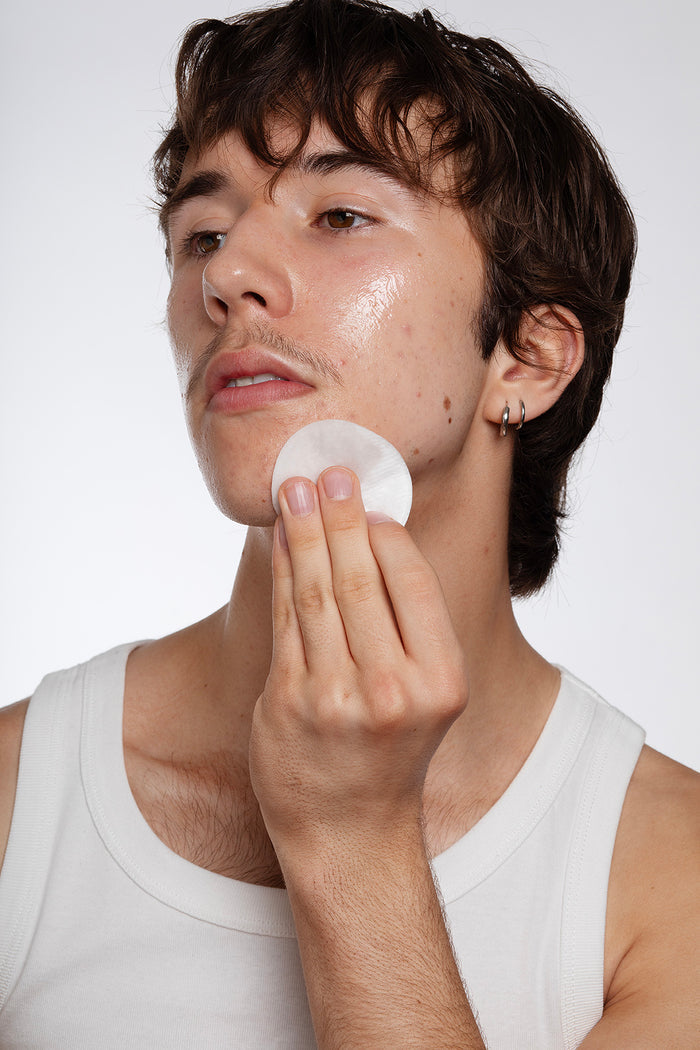 Boy applying Common Clouds Cloud Water BHA toner to his face with a cotton pad.