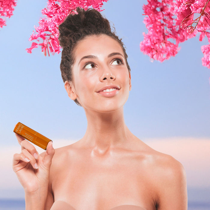 Woman holding France Laure Revolusolive complexion corrector under pink blossoms, showcasing radiant skin and natural beauty