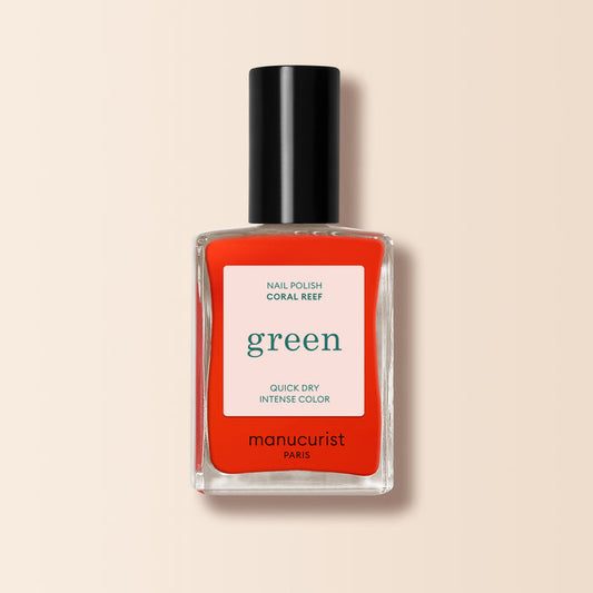 A bottle of Manucurist Coral Reef nail polish, a vivid coral shade with a black cap and white label displaying green and red text, shown on a light beige background.