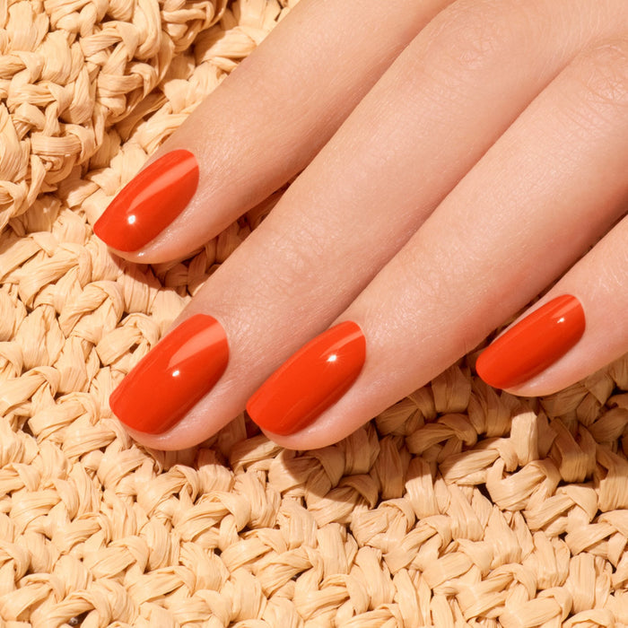 A hand with neatly manicured nails painted in Coral Reef nail polish from Manucurist’s Green™ range rests on a woven beige textured surface.