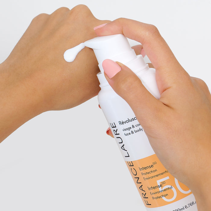 Hand applying white cream from a bottle labeled 'Intense 50 Environmental Protection' for face & body skincare.