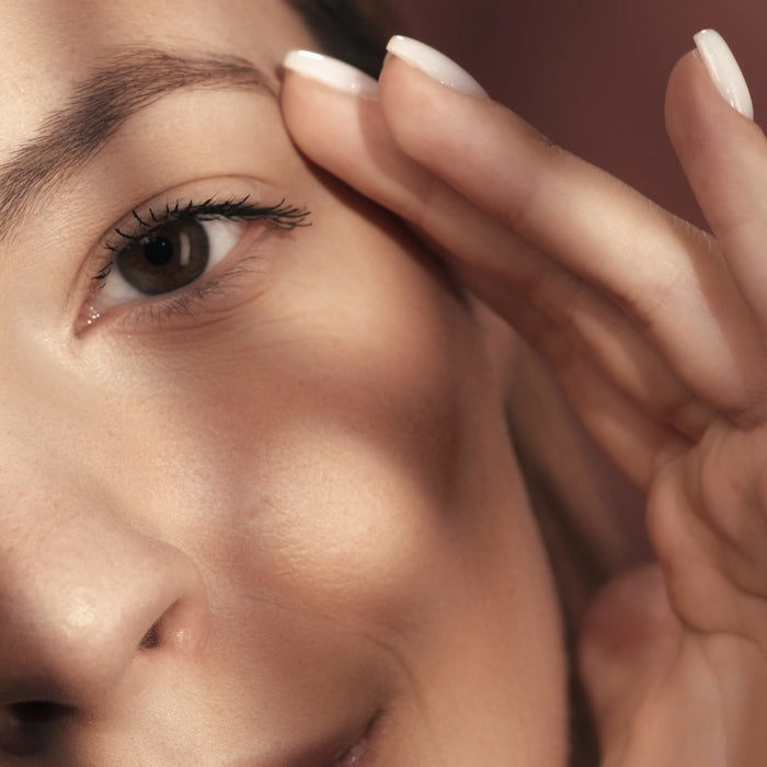 Woman gently applying eye cream to delicate under-eye area, showcasing smooth skin texture and natural beauty routine