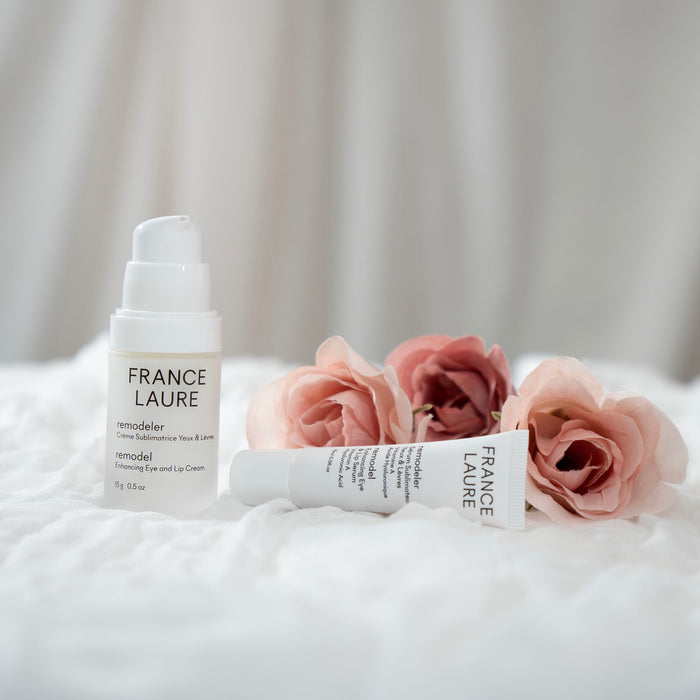 France Laure Remodeler Enhancing Eye and Lip Cream with serum tube, displayed on white fabric beside soft pink roses for luxury skincare.