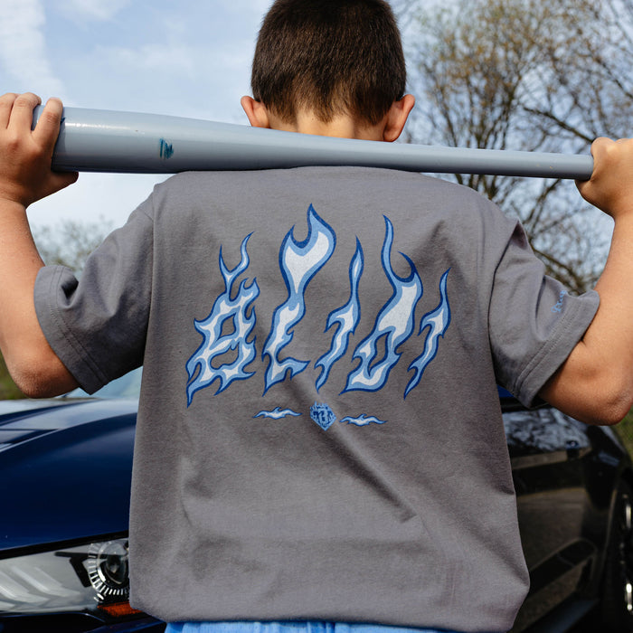 Back view of gray youth Flame Thrower tee with blue and white BL101 flame letter graphic, boy holding bat across shoulders beside navy car.