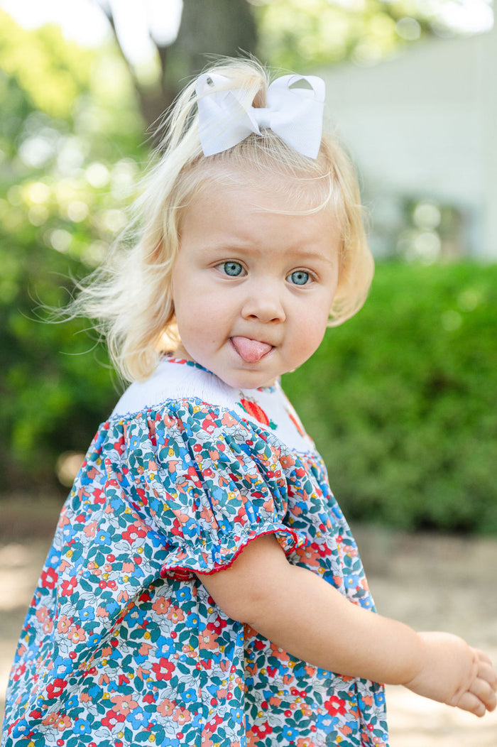 Close-up side profile of baby girl in Smocked Floral Pumpkin Bloomer Set by Ruth and Ralph, blue floral print with white bow