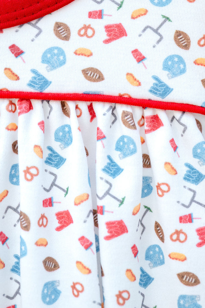 Girl's white game day dress with football and tailgate print, styled with pom-poms and a football for game day