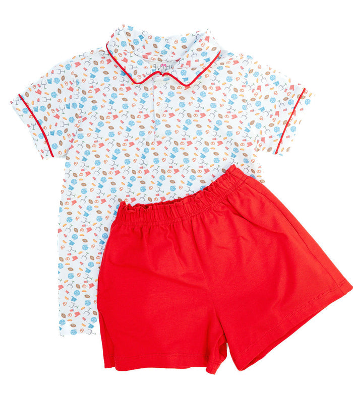 Young boy modeling a white and red game day polo set with football motif print, holding a Wilson football in a park