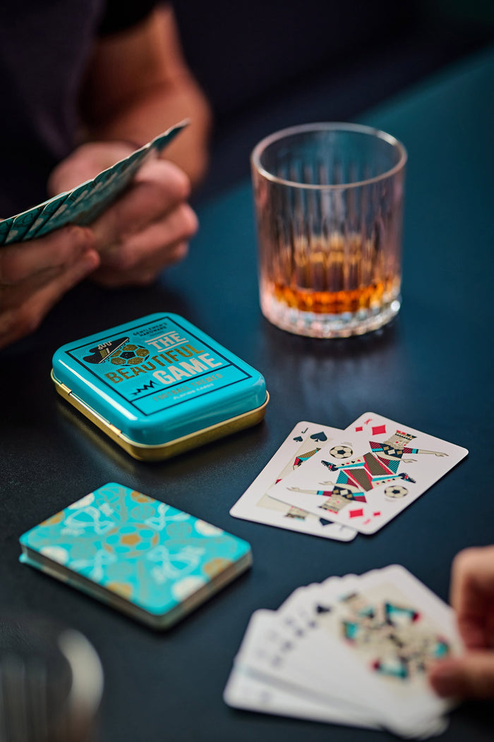 Football-themed playing cards with teal tin and face-up cards, played by hands on table.