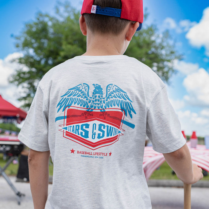 Freedom Swings Tee - Heather Gray: Back view of youth male model showing Stars and Swings eagle graphic on heather gray tee at outdoor baseball event