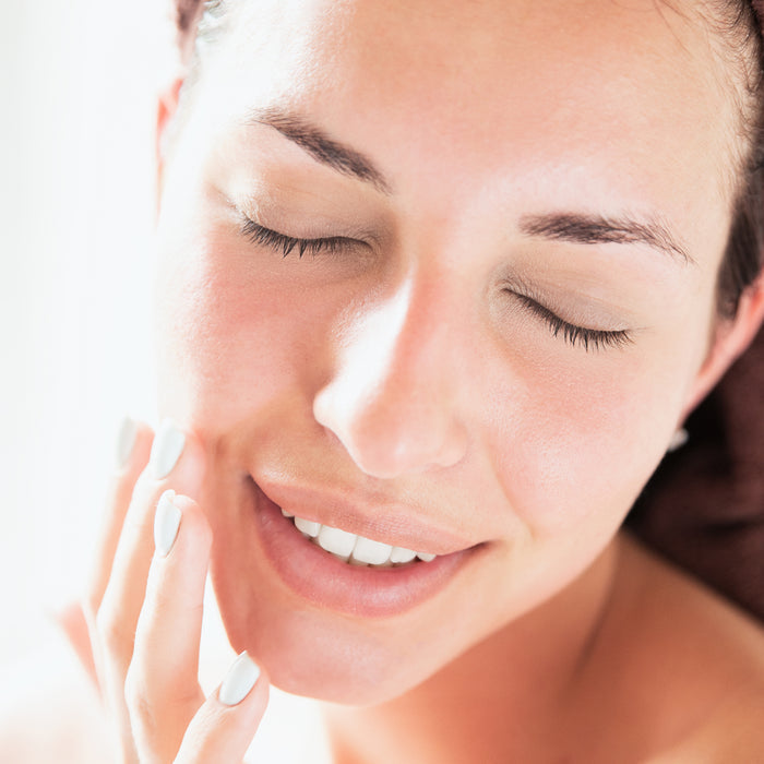 Woman gently touching smooth, radiant skin with eyes closed, showcasing natural beauty and skincare results for all skin types.
