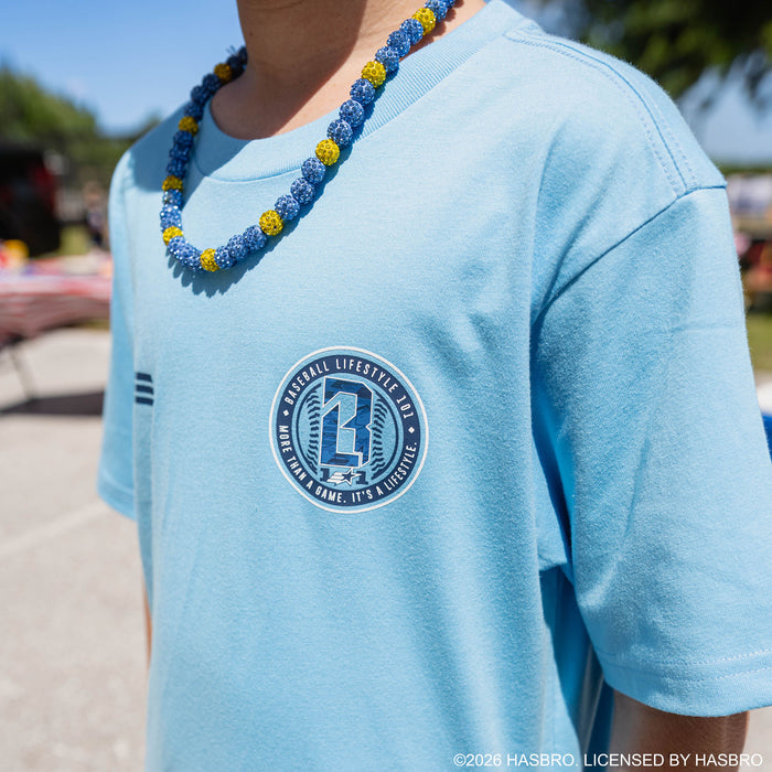 Close-up of youth model in light blue GI Joe tee showing large circular Baseball Lifestyle 101 badge on chest