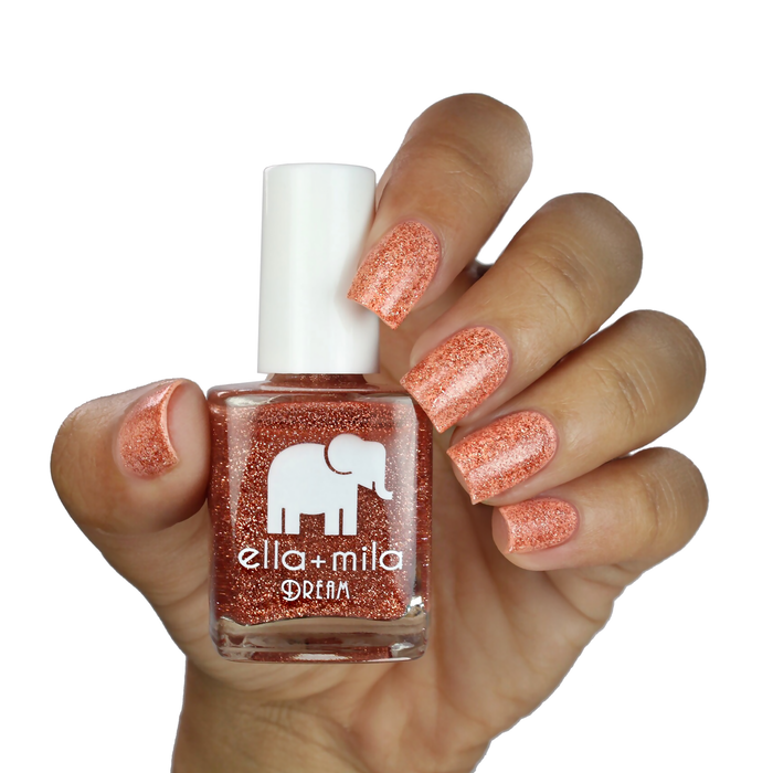 Glow With Me bronze glitter nail polish on a medium skin tone, hand holding the bottle