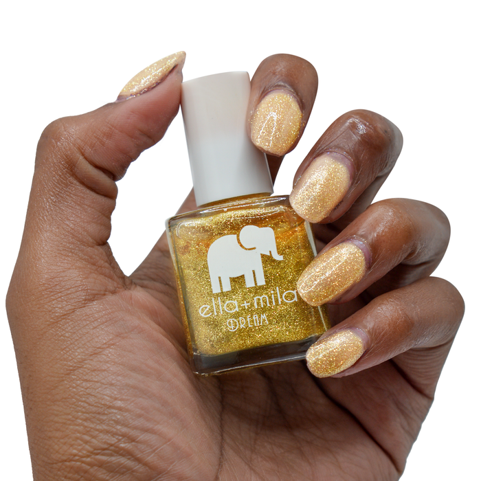 Golden Fairy gold glitter nail polish on a deep skin tone, hand holding the bottle