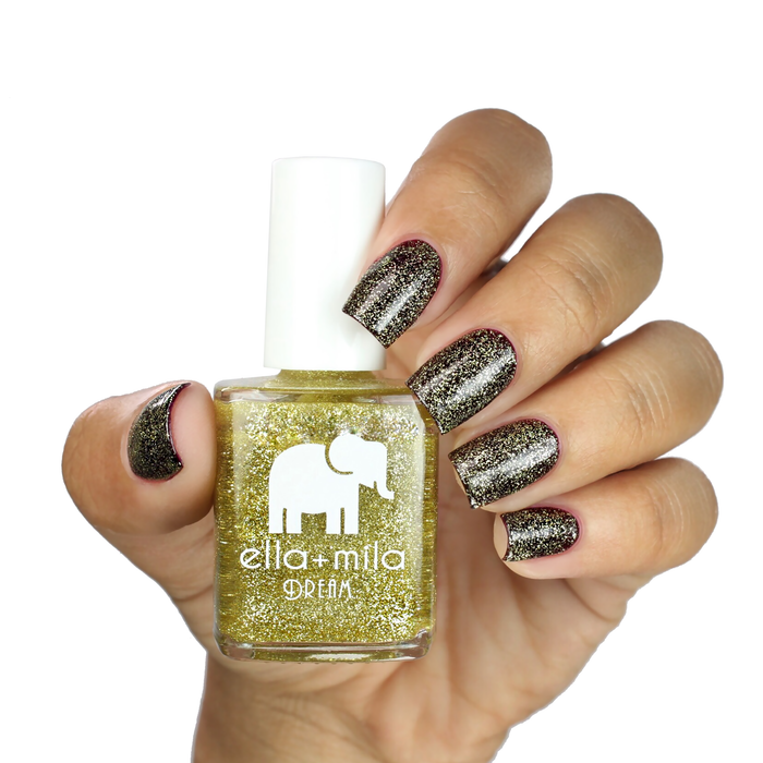 Golden Fairy gold glitter nail polish alternating with black on a medium skin tone, holding the bottle