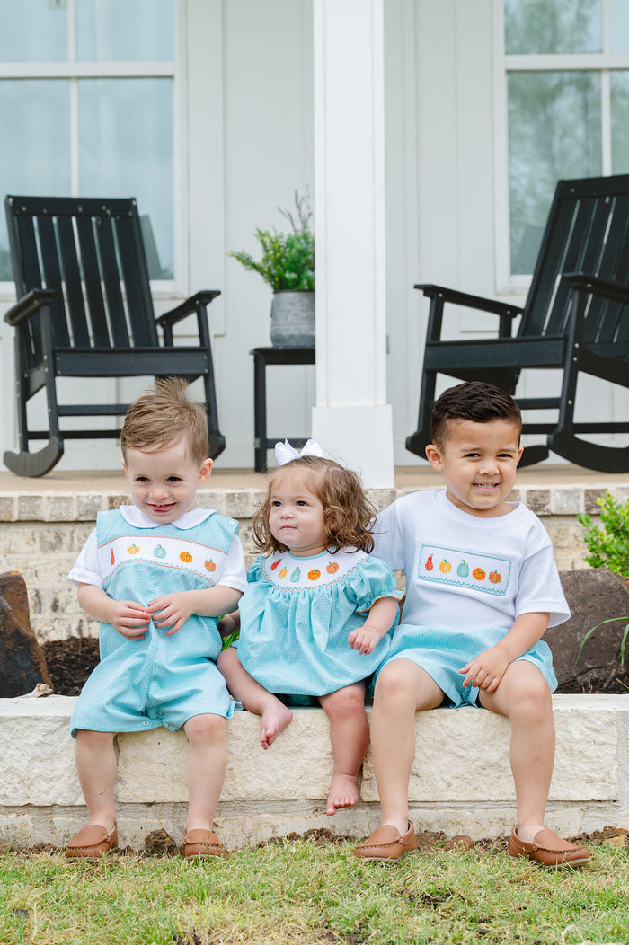 Three children sitting outdoors wearing matching Ruth and Ralph smocked fall gourds outfits