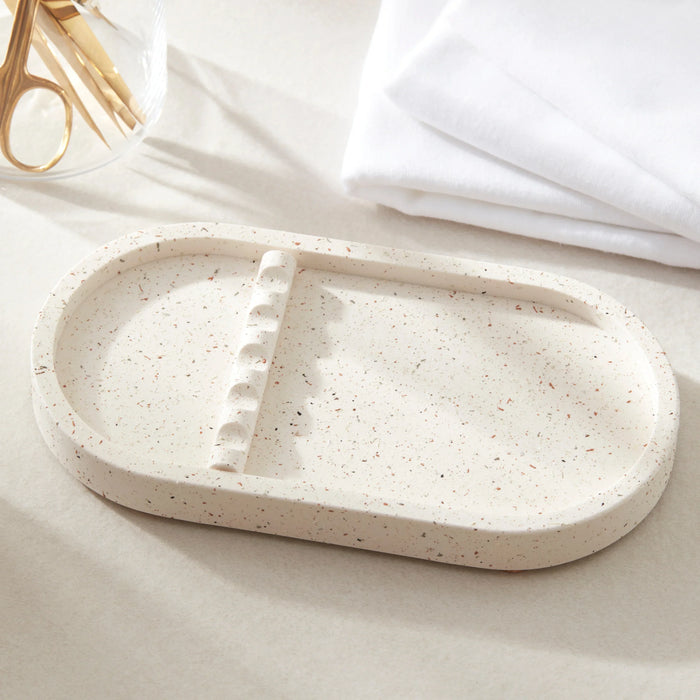 Speckled beige ceramic tray on a light surface with white cloth and gold scissors in the background.