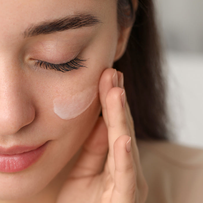 Woman applying gentle face cream to cheek, showcasing smooth skin texture and natural skincare routine for all skin types.