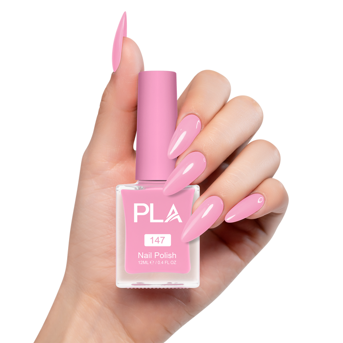 Hand holding a pink nail polish bottle with matching nails on a white background