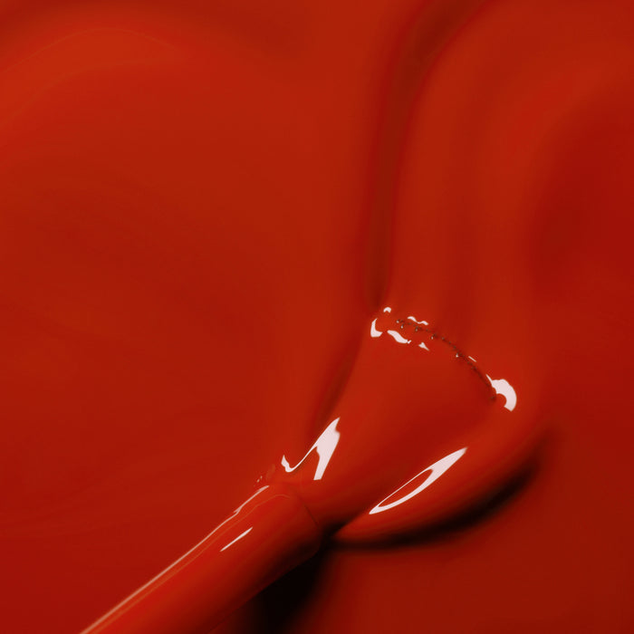 A close-up of the Manucurist Indian Summer nail polish brush coated in glossy ochre red, resting on a smooth, reflective surface matching its vibrant shade.
