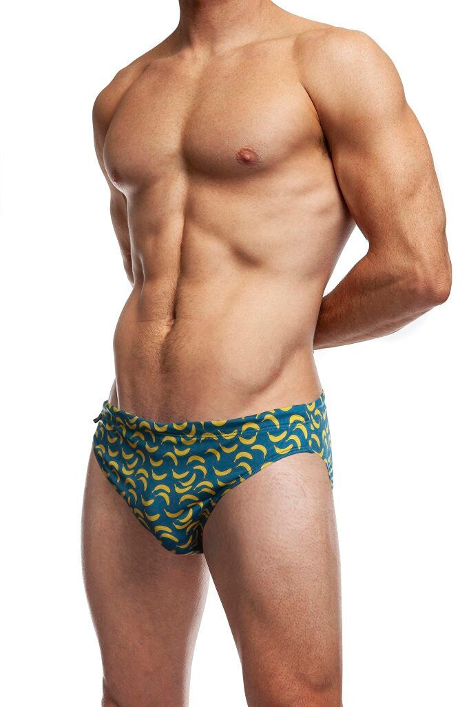 Man standing wearing a pair of Jack Adams indigo IT's Bananas Swim Brief (profile view) on a white background.