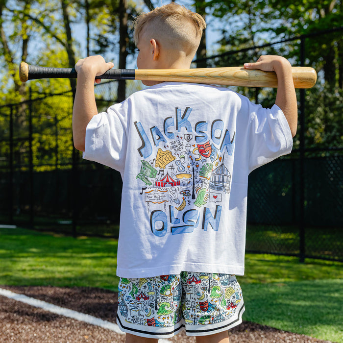 Back view of the white youth Jackson Olson x BL101 relaxed tee showing the large "Jackson Olson" graphic with colorful illustrated artwork and "That's Show Biz, Baby" text