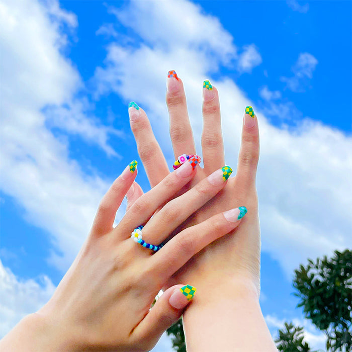 Hands with blue geometric press on nails and colorful checker designs against bright sky
