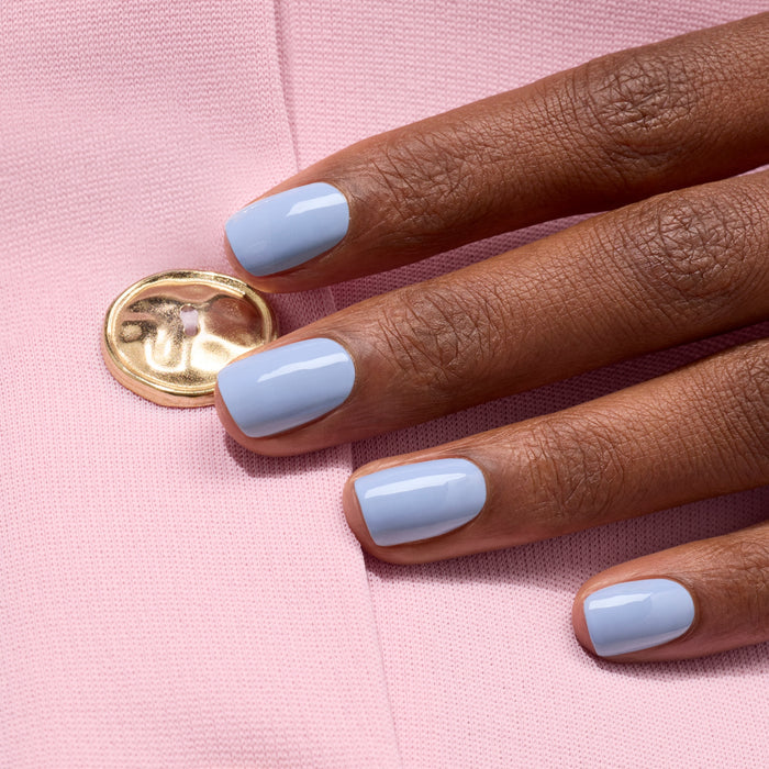 A hand with neatly manicured nails painted in Manucurist’s glossy mauve Lilas shade rests on pink fabric with a gold button.