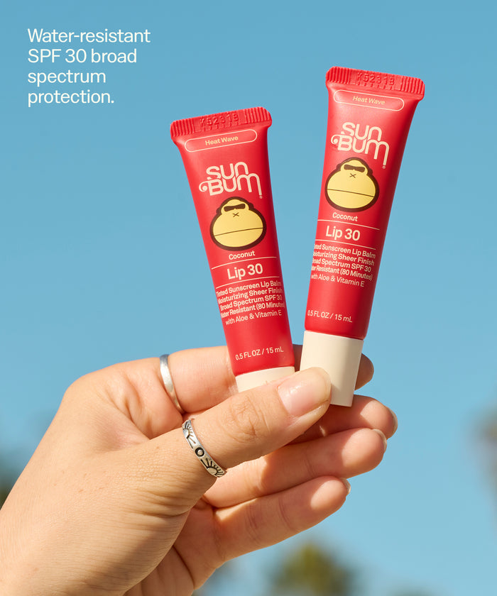 Hand holding two Sun Bum Lip 30 Duo: Heat Wave + Heat Wave tubes with SPF 30 against blue sky. Water-resistant
SPF 30 broad spectrum protection.