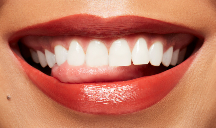 M.A.C Lustreglass Sheer-Shine Lipstick in Chili Popper, showing a close-up of the vibrant coral lipstick on lips.